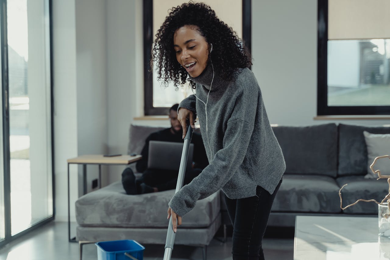 A cheerful young woman mopping the floor in a cozy, modern living room.